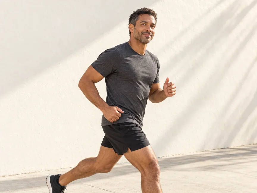 A fit man in his early forties jogging past a sunlit white wall