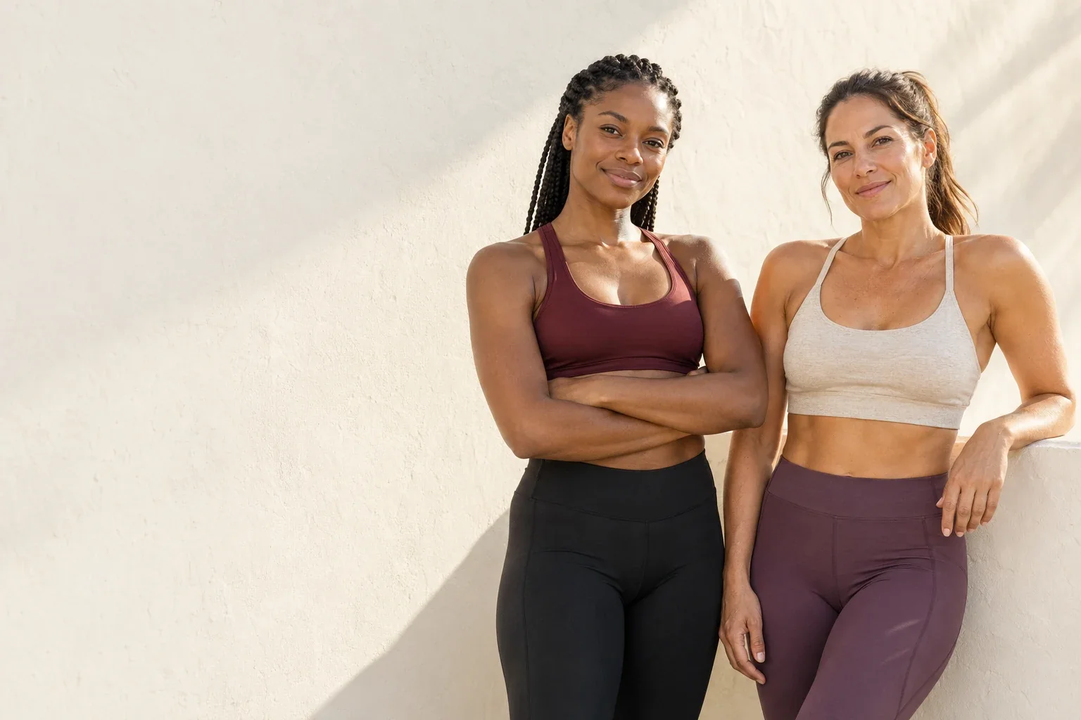 Two fit women in sports bras and leggings smiling in warm morning sunlight